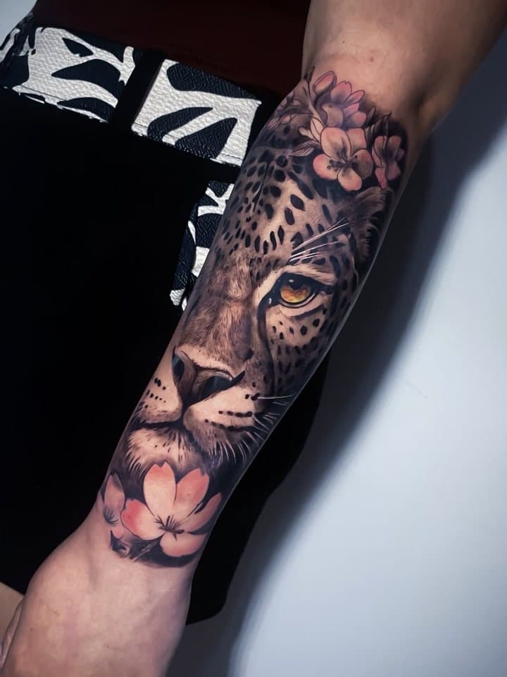 Tatuagem realista de onça com cerejeiras no antebraço